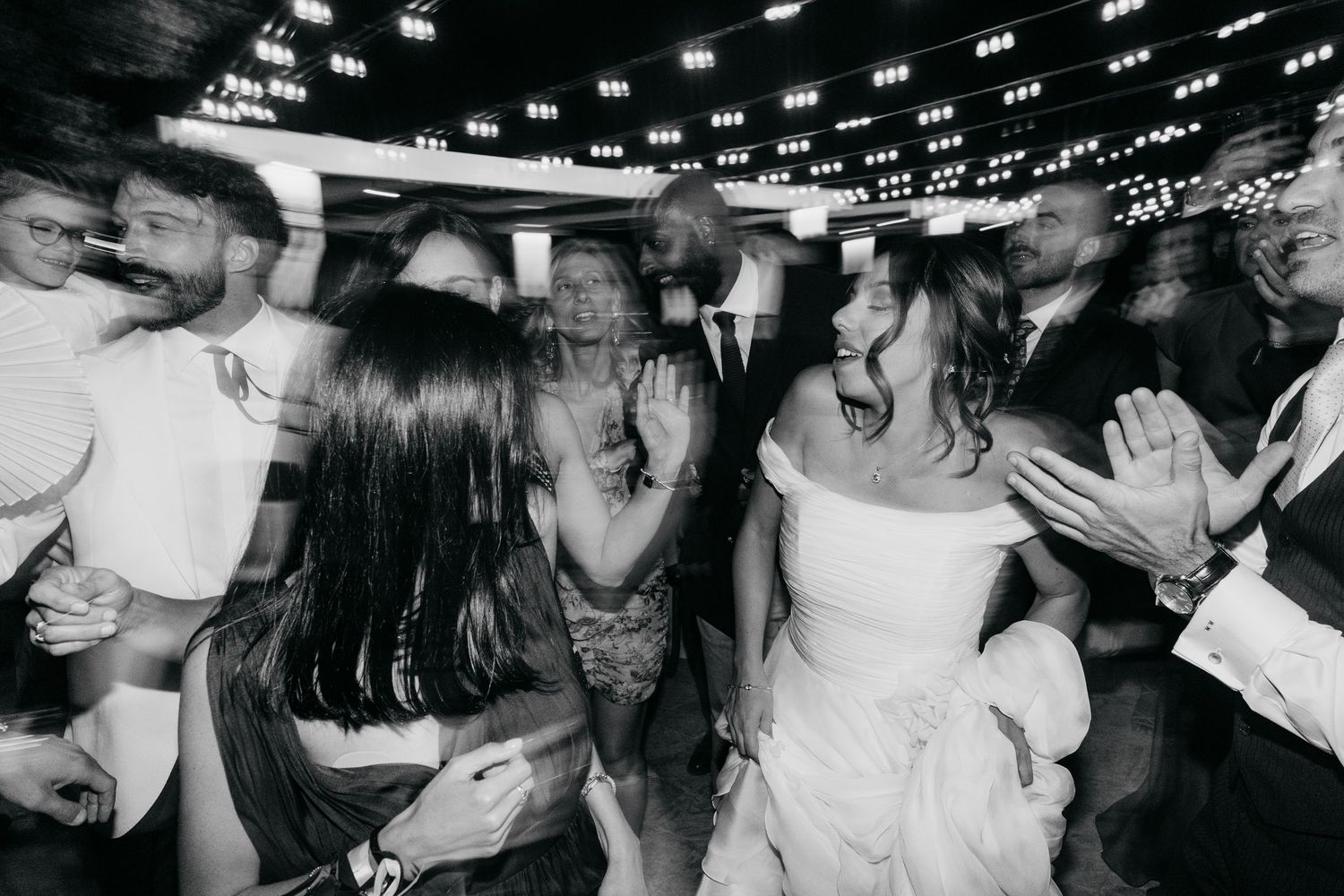 Energetic party guests dancing under string lights at a celebratory event.