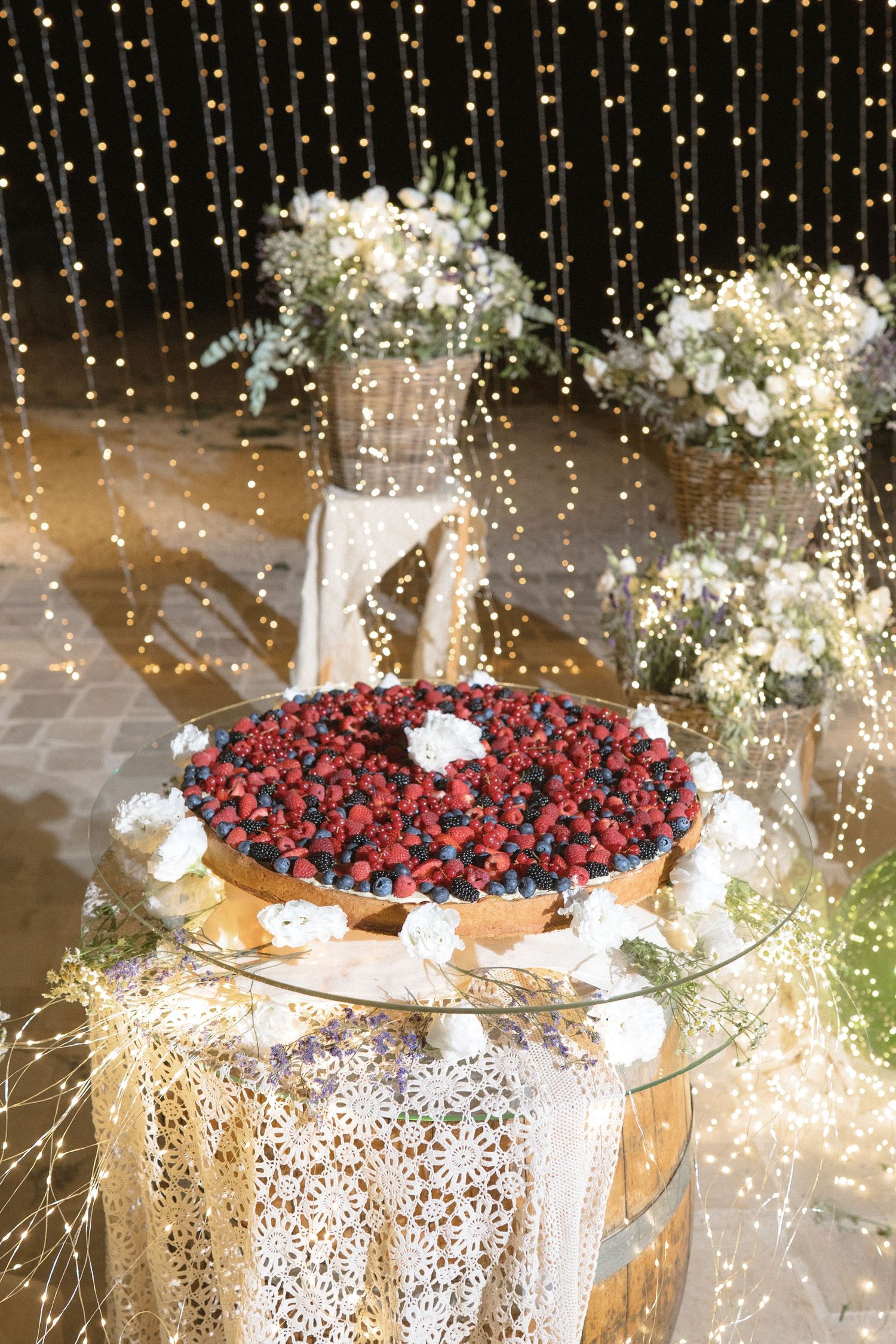 A beautifully decorated dessert table with sparklers and mixed berries arranged on white lace tablecloths.