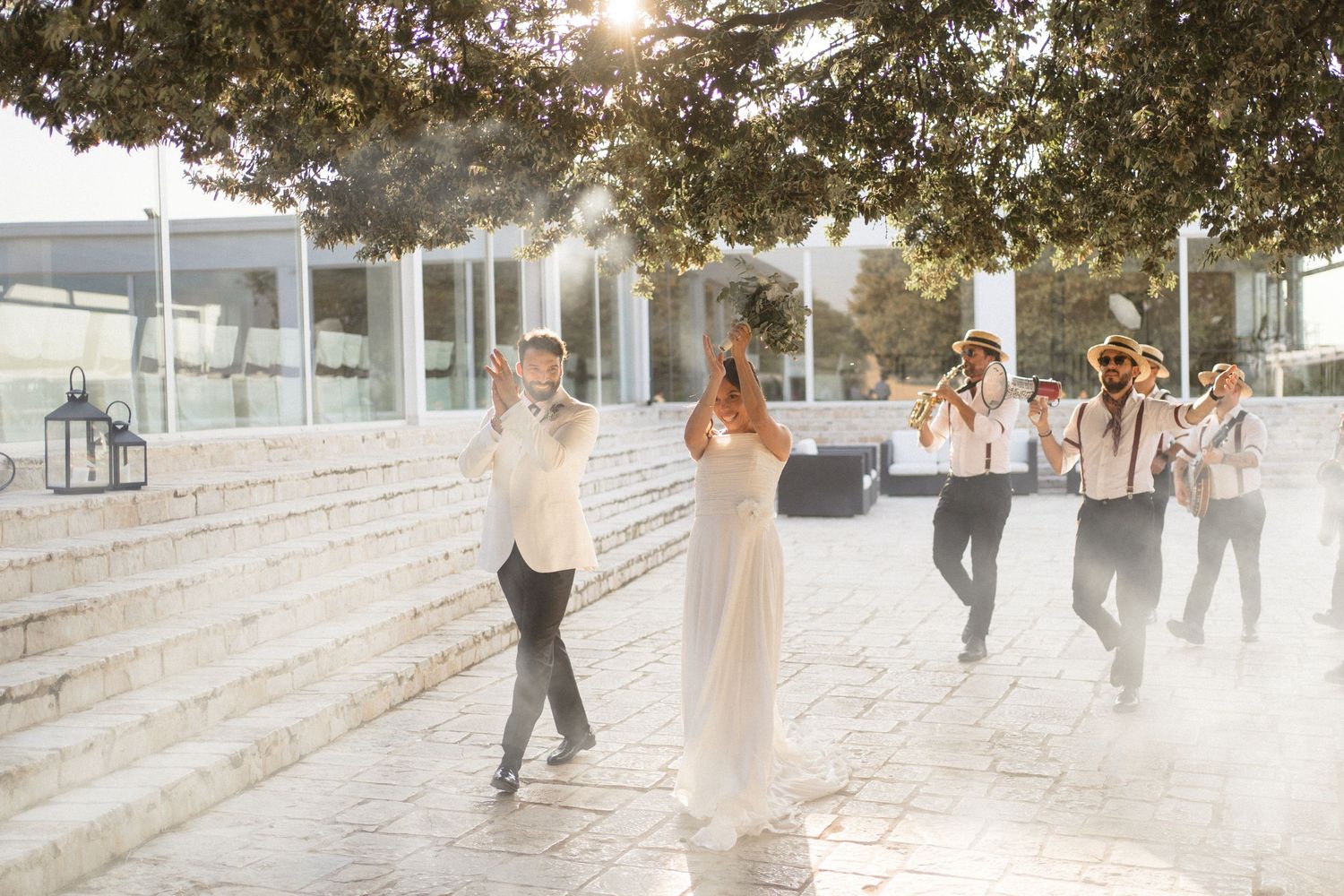 Wedding party dances joyfully on a stone patio during sunset celebrations.