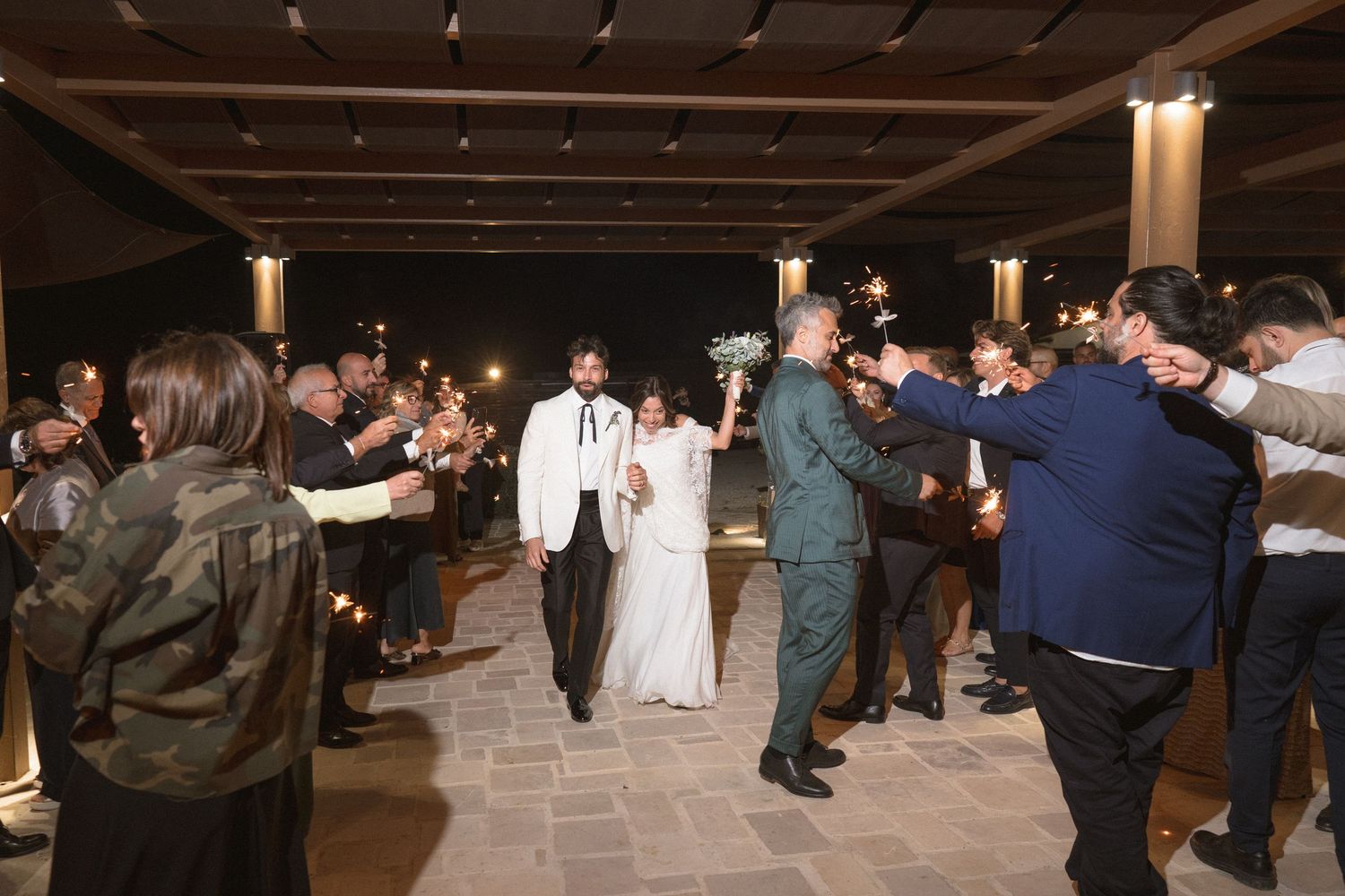Wedding guests dancing on wooden floor under string lights and rustic ceiling beams.