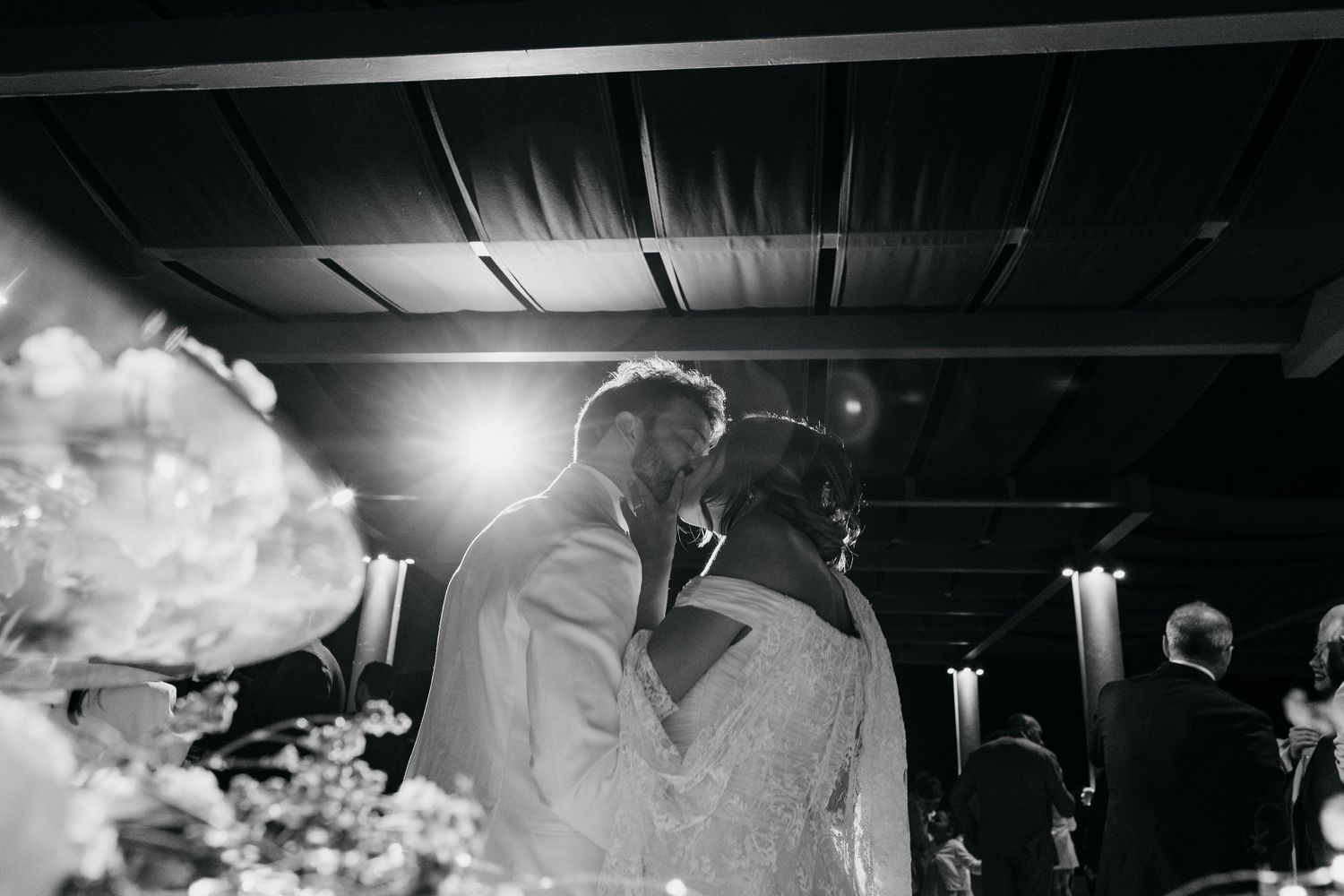 Black and white photo of wedding guests dancing in a dimly lit reception venue.