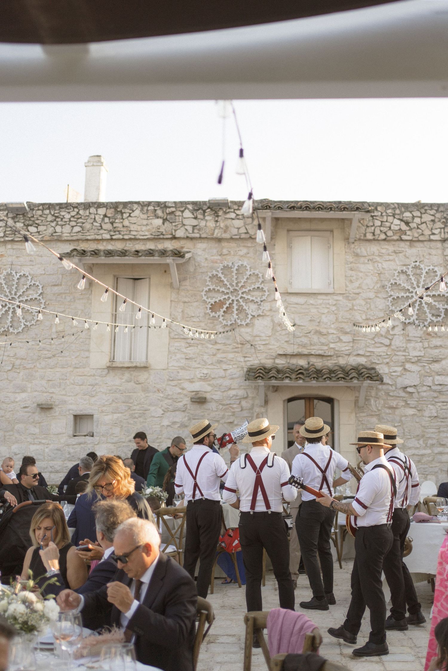 Wedding guests in vintage attire dancing in front of a stone wall at an outdoor reception.
