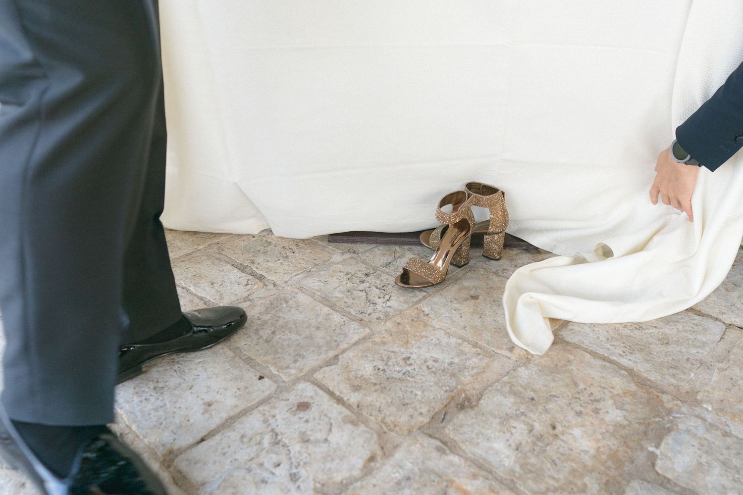 A dog rests on stone flooring between formal attire at an event.