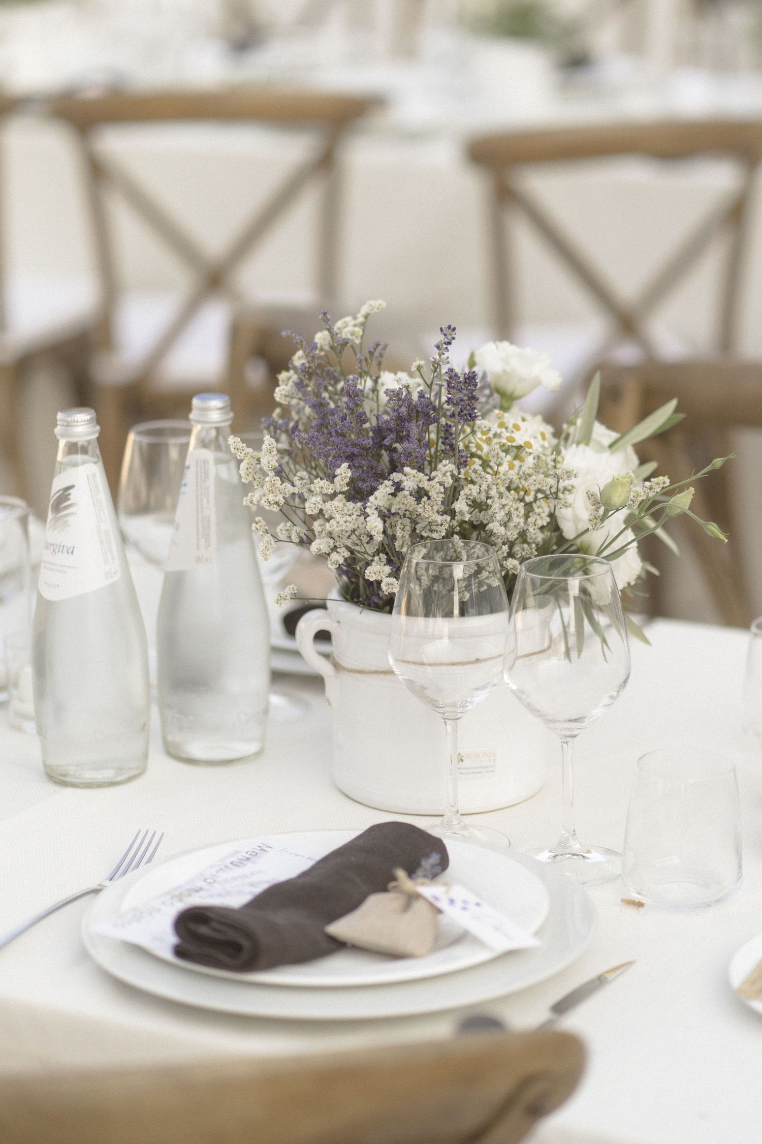 Elegant wedding table setting with glass bottles, floral arrangements, and white tableware in natural light.