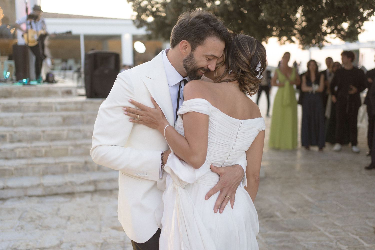 Couple in white wedding attire dancing together during a romantic outdoor celebration.