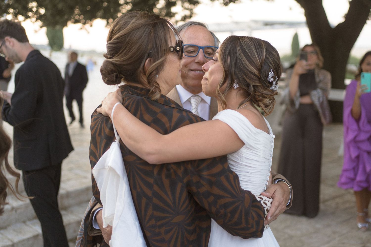 Couples dancing and embracing at an outdoor wedding reception under trees.