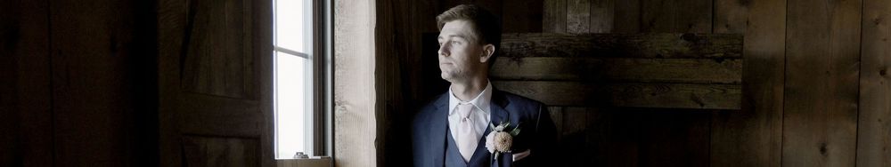Person standing in formal attire near a window in a rustic rustic building.