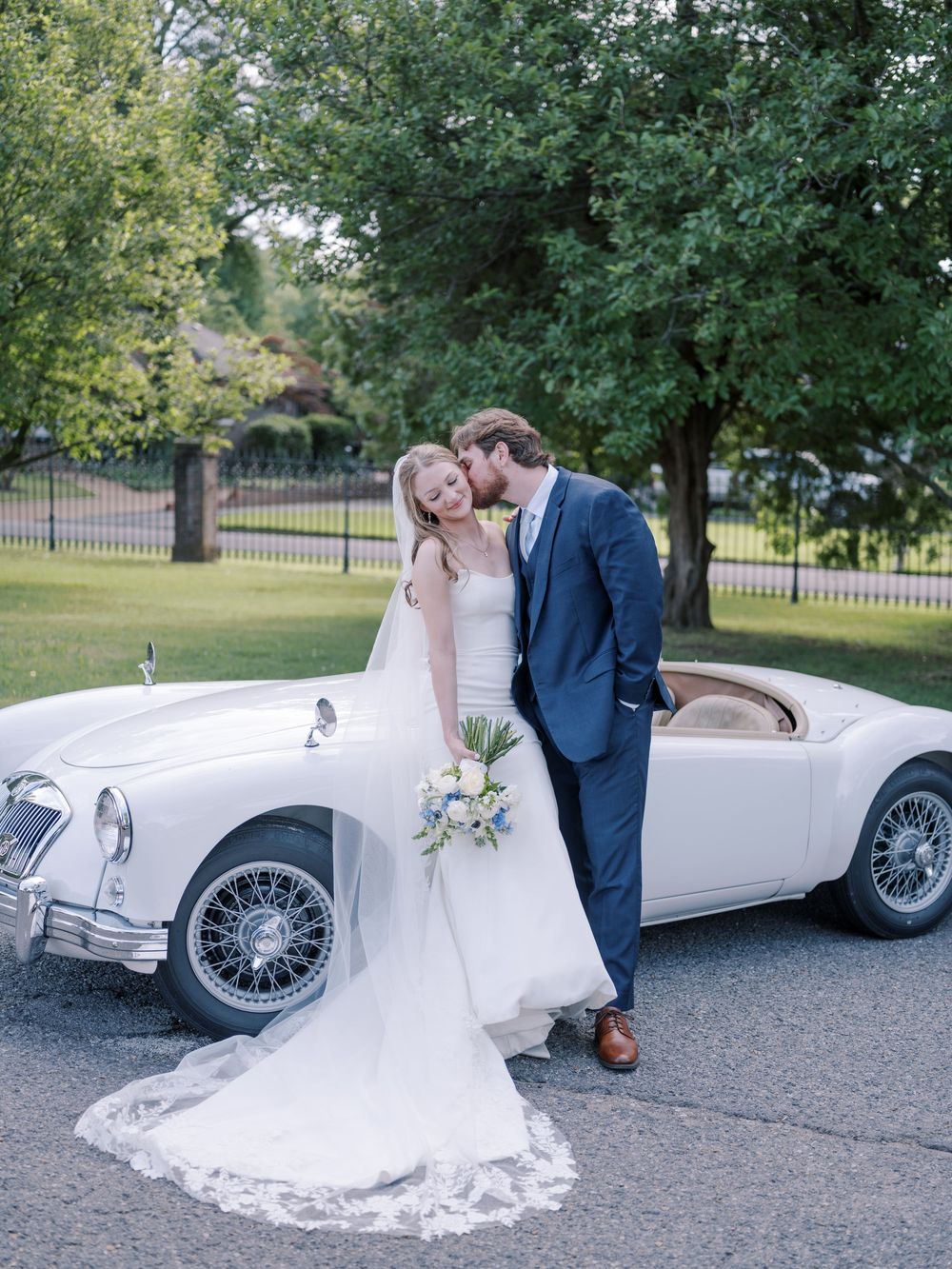 A couple poses with a classic white vintage MG sports car at their wedding celebration.