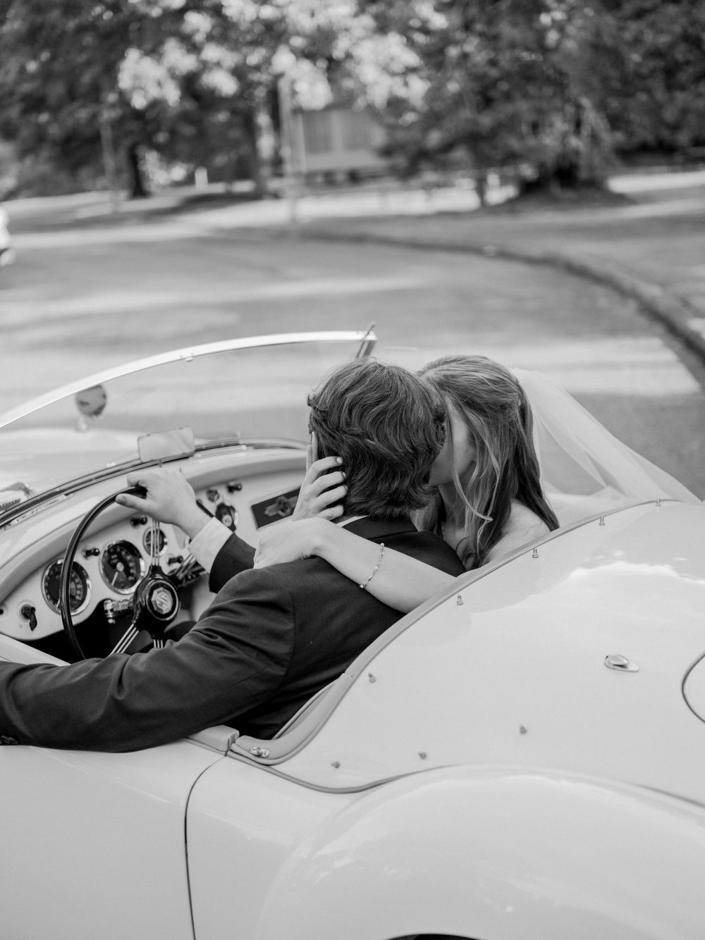 A romantic black and white photograph showing a couple embracing in a vintage convertible sports car.