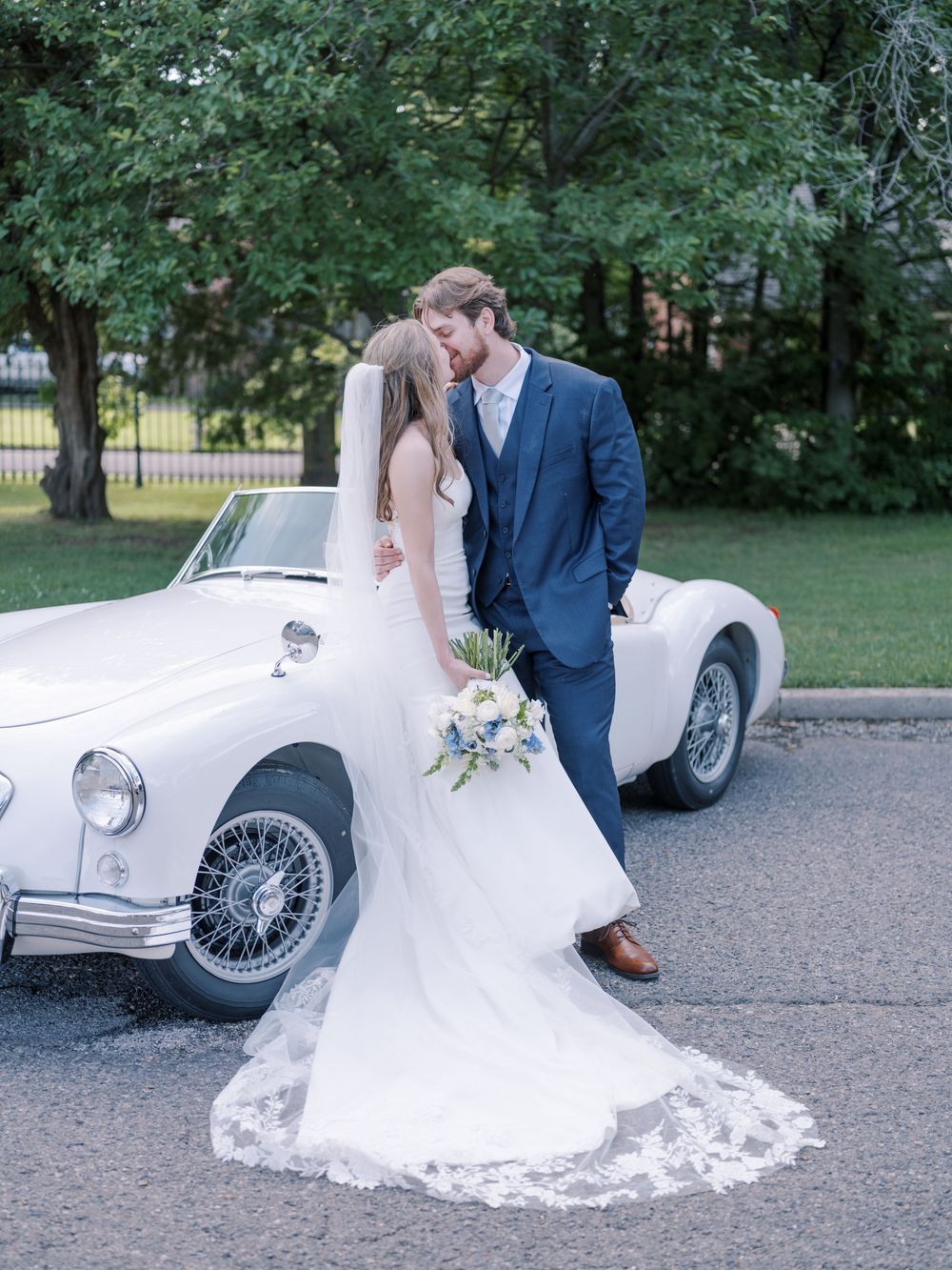 A vintage white classic car serves as backdrop for newlyweds sharing a romantic moment on their wedding day.