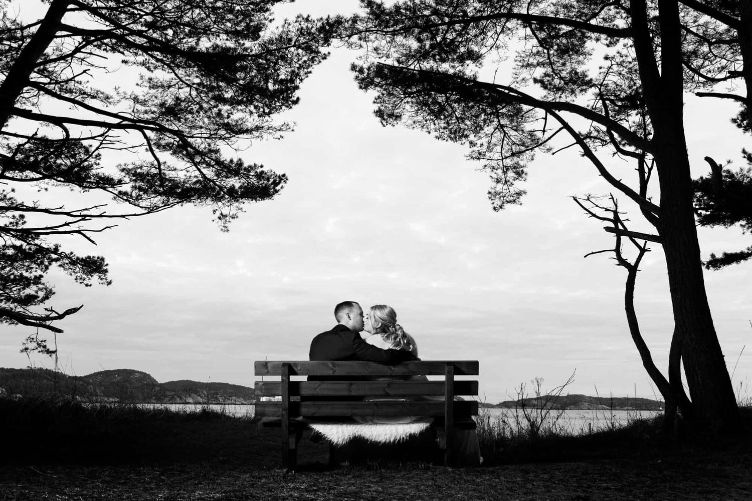 brudepar sittende på benk som kysser og ser ut utover vannet Sjøsandenpå bryllupsfotografering i Mandal