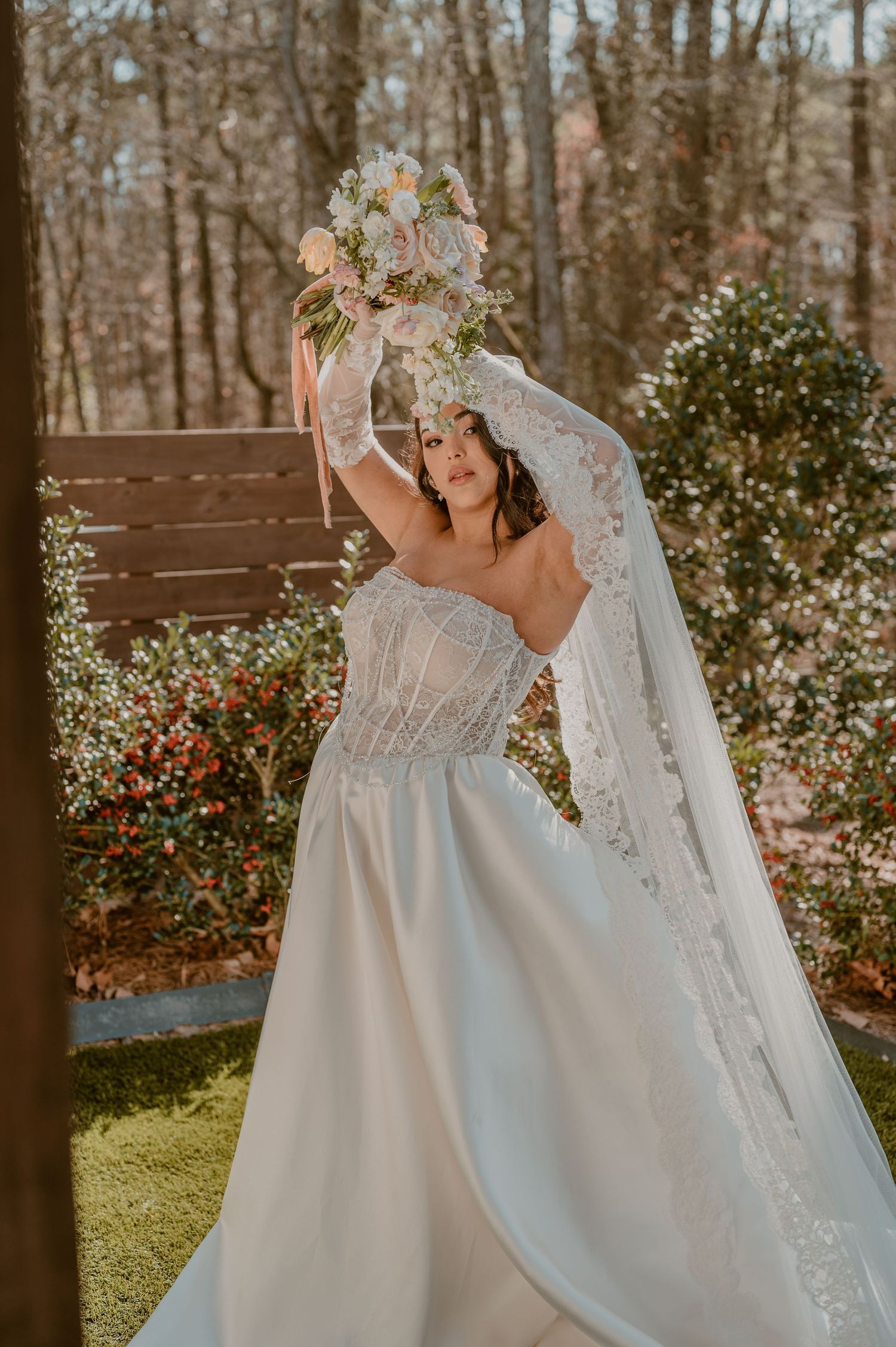 Beautiful wedding dress with beaded bodice and flowing skirt shown in outdoor garden setting with floral bouquet and veil.