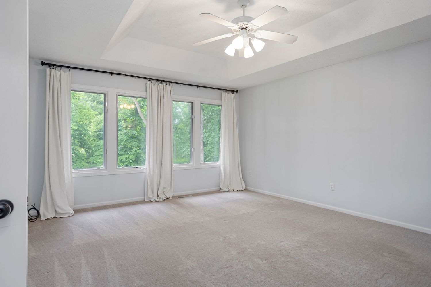 Bright room with white curtains, ceiling fan, and large windows overlooking lush greenery.