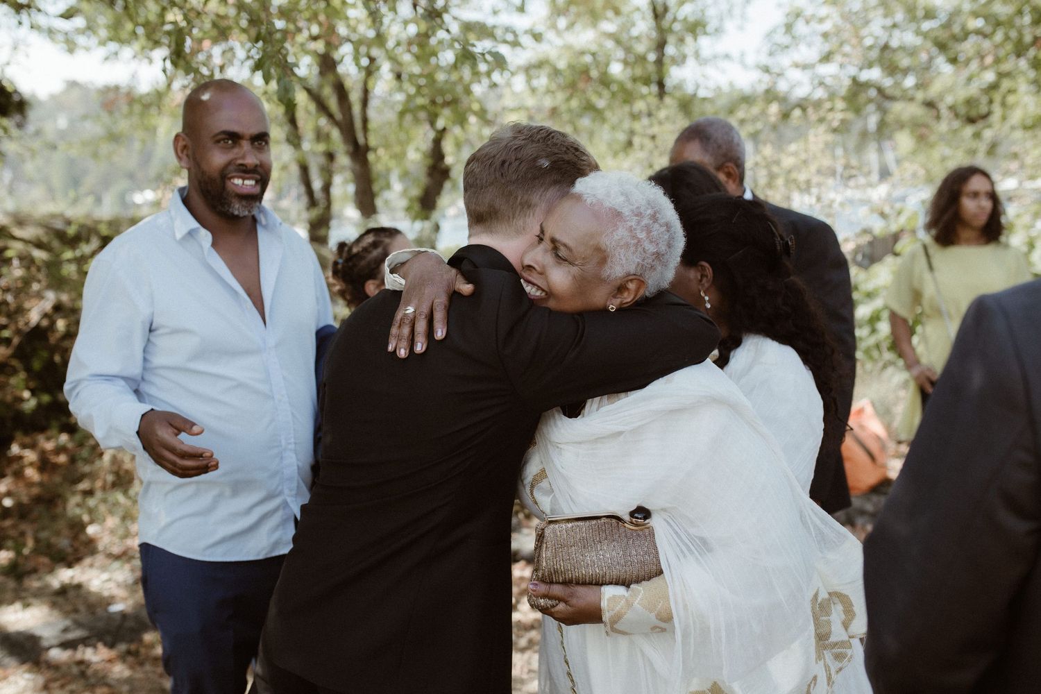 Family members share a warm embrace at an outdoor gathering while others look on in the background.