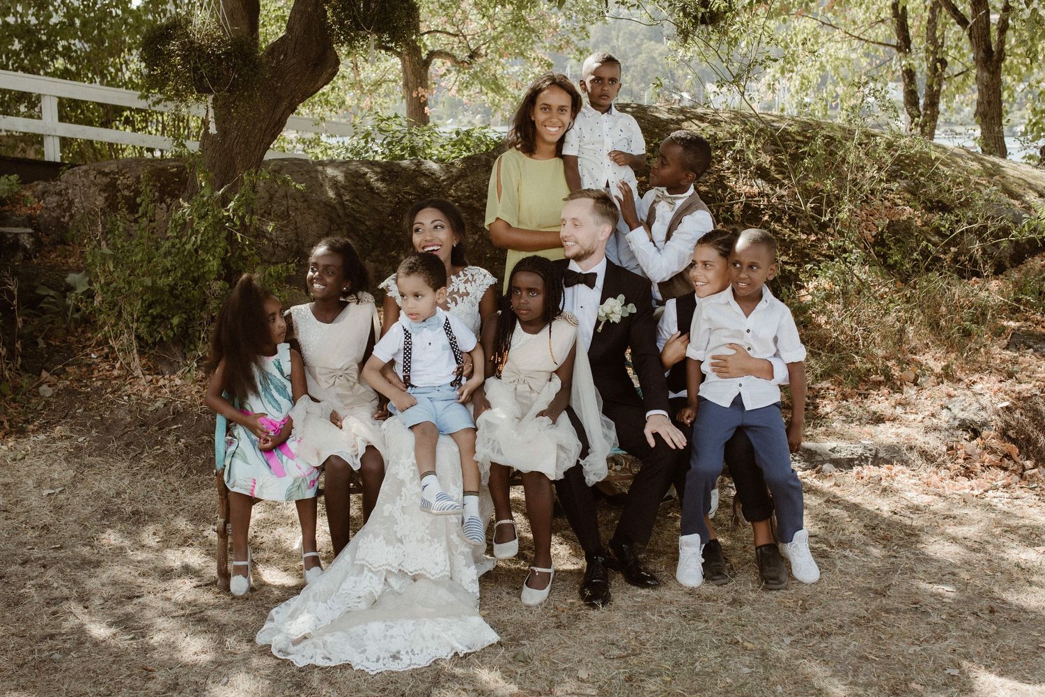 Group photo outdoors with people gathered around someone in a white wedding dress in a natural setting.