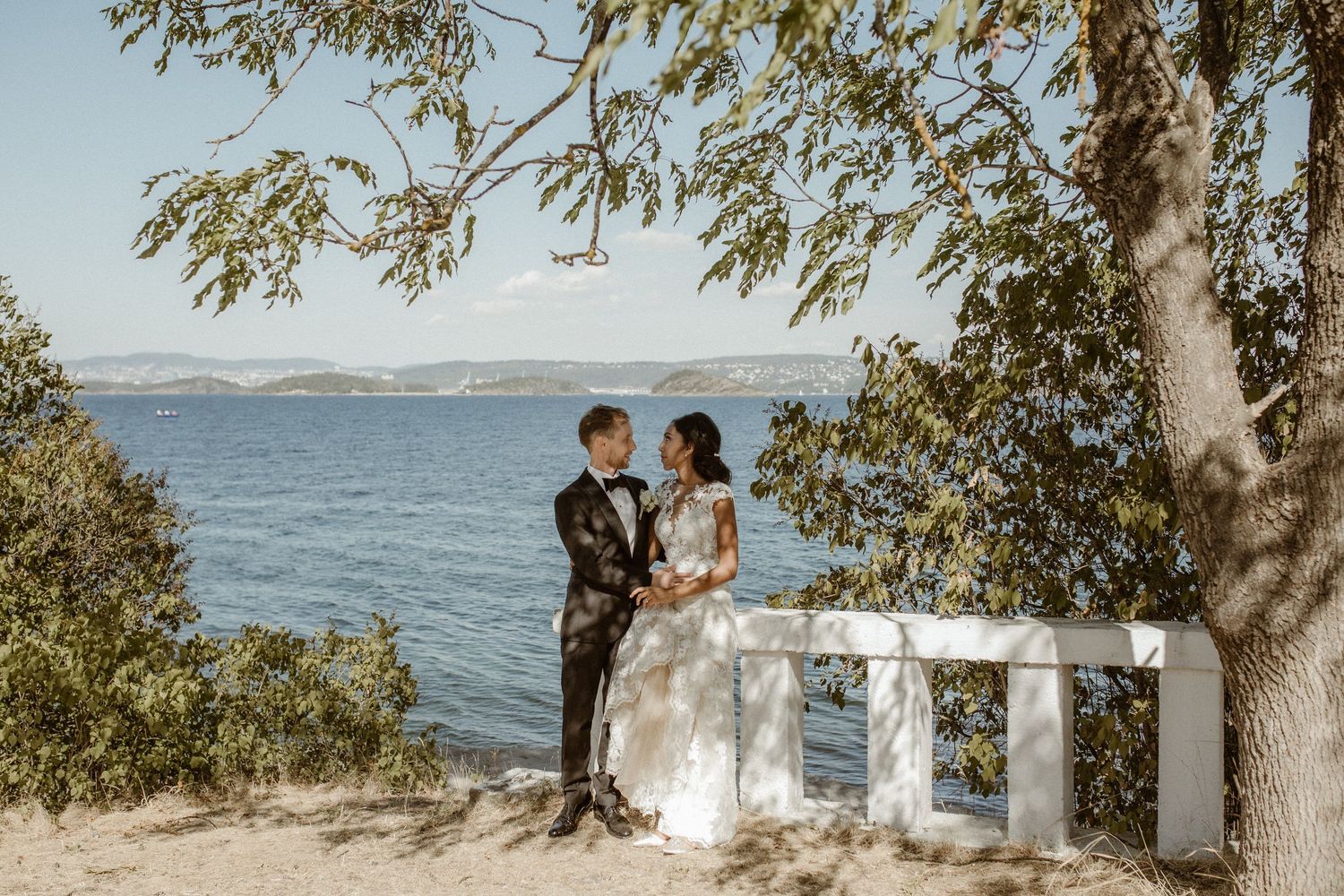 A wedding couple poses together on a stone overlook with a scenic ocean view.