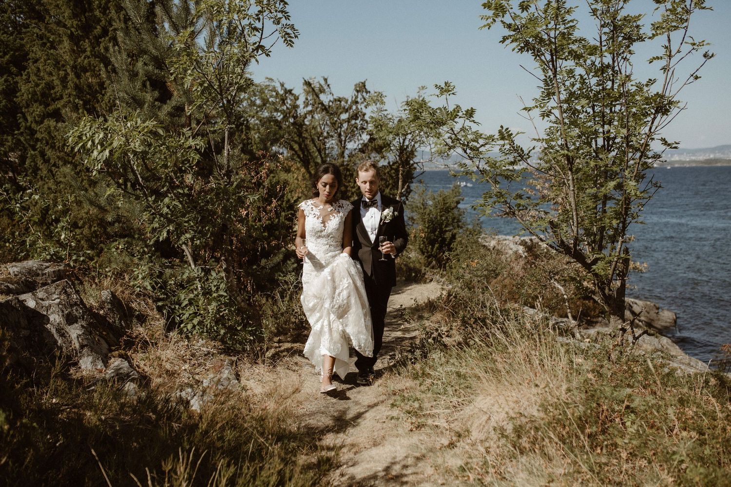 Couple walks along coastal cliff path with ocean views on their wedding day.