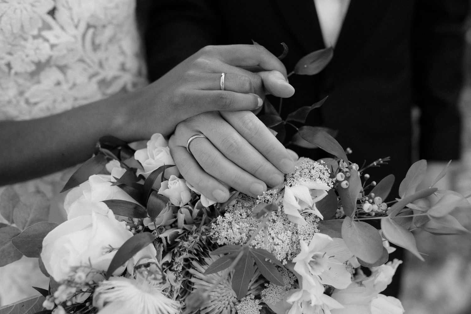 Close up of wedding rings and delicate white floral bouquet arrangement.