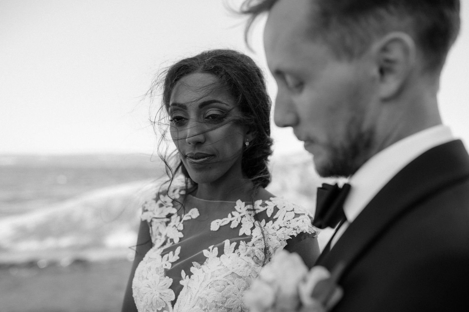 Artistic black and white portrait of a couple in wedding attire by the ocean.
