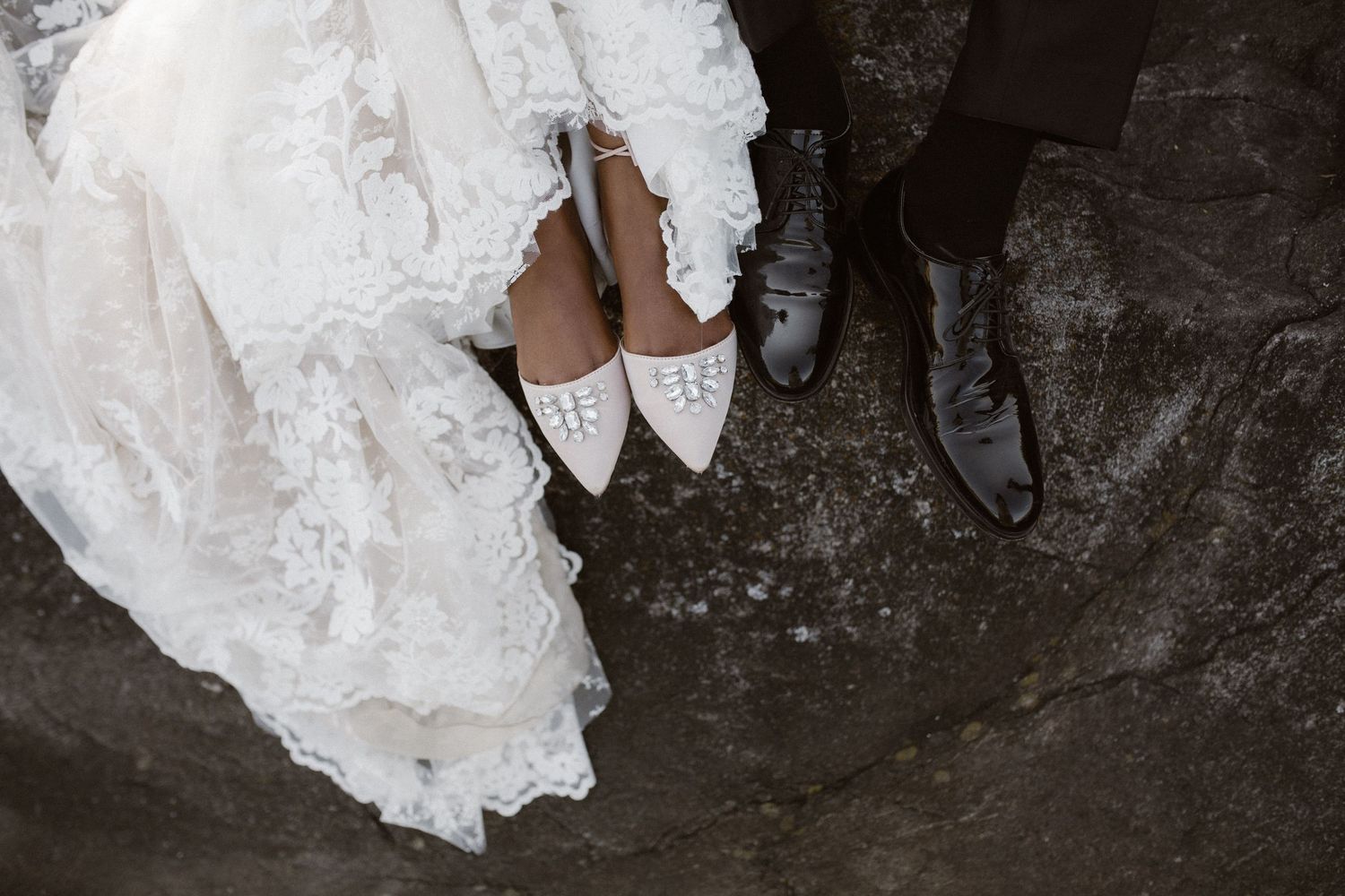 Wedding shoes detail shot showing bride's white lace flats next to groom's formal black shoes.