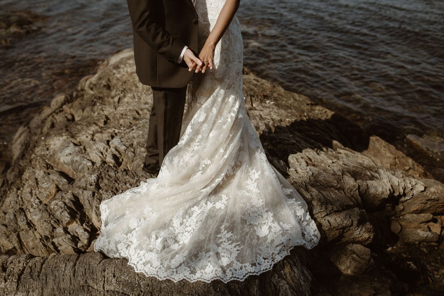 Wedding dress train with intricate lace detail spread across rocky coastal setting.