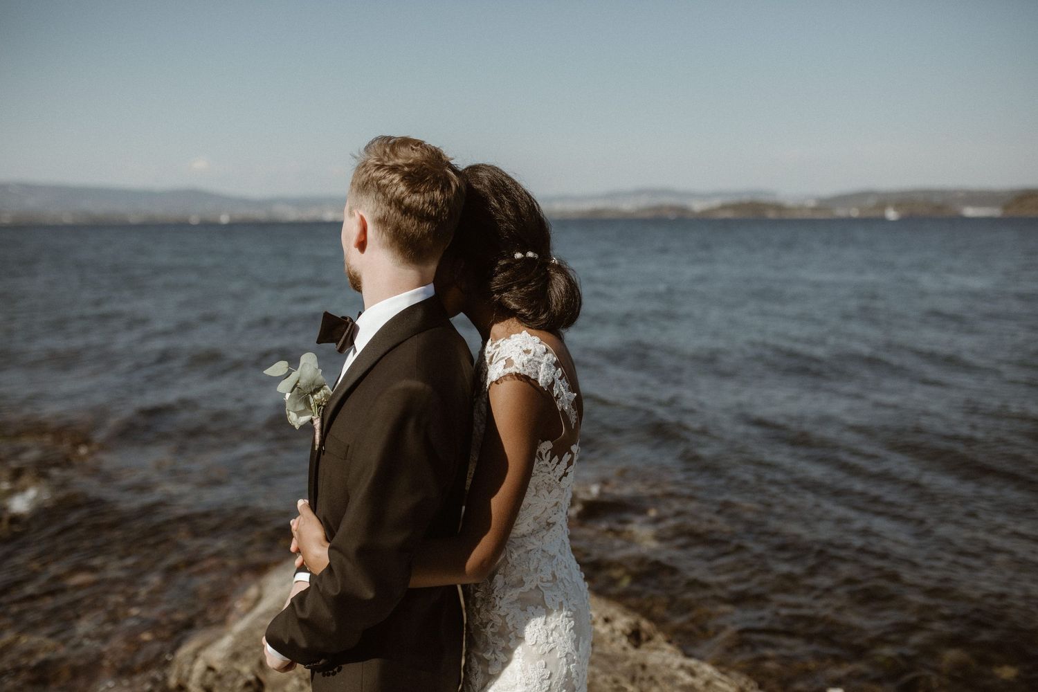 A newlywed couple shares an intimate moment on rocky coastline overlooking the sea.