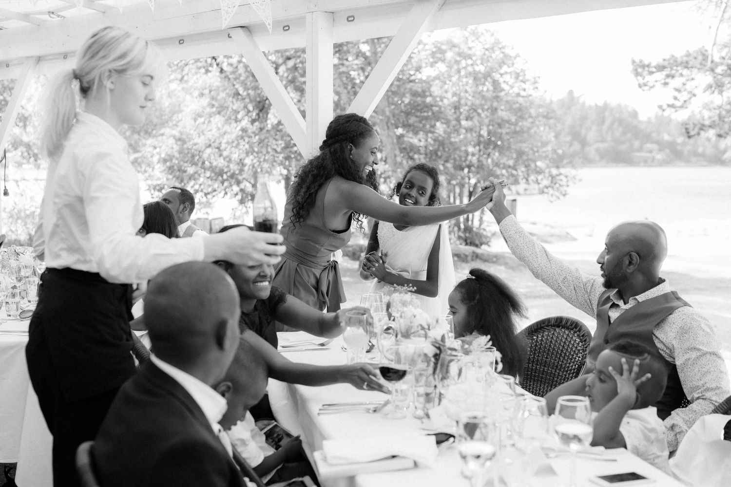 Guests enjoying an elegant outdoor reception dinner under a white pergola by the water.