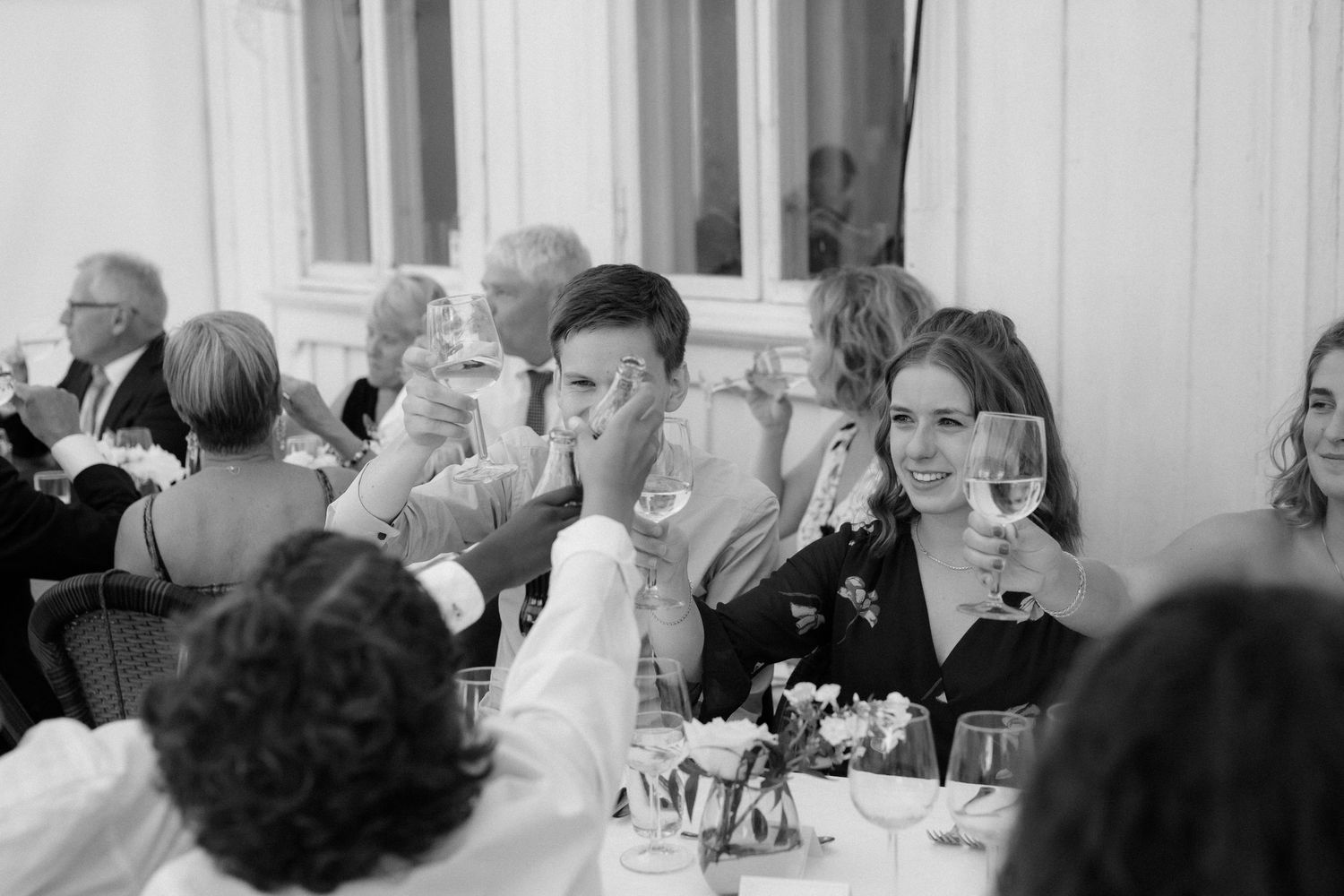 Black and white photo of wedding guests toasting during dinner reception.