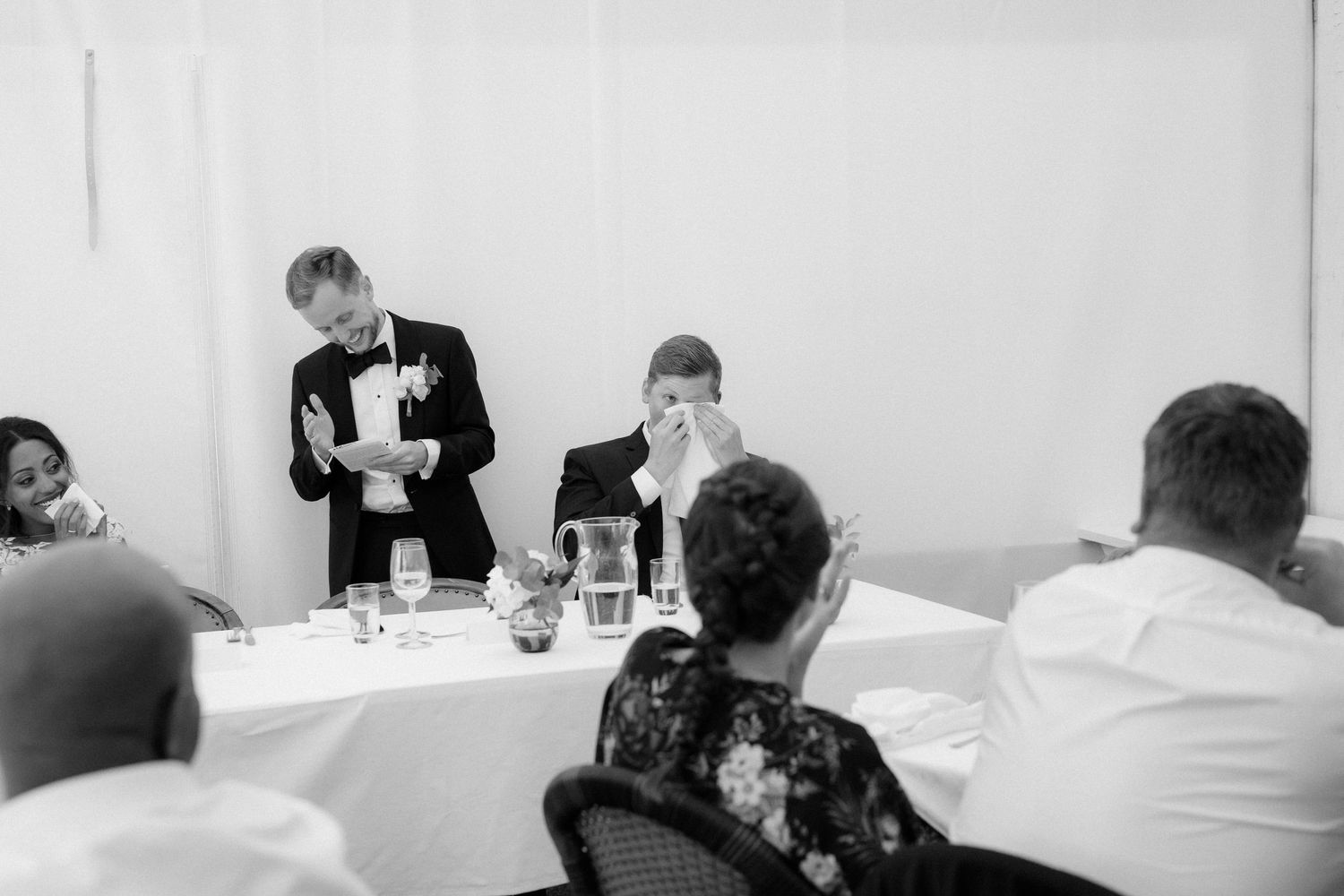 Black and white photo of guests seated at tables during an indoor wedding reception.