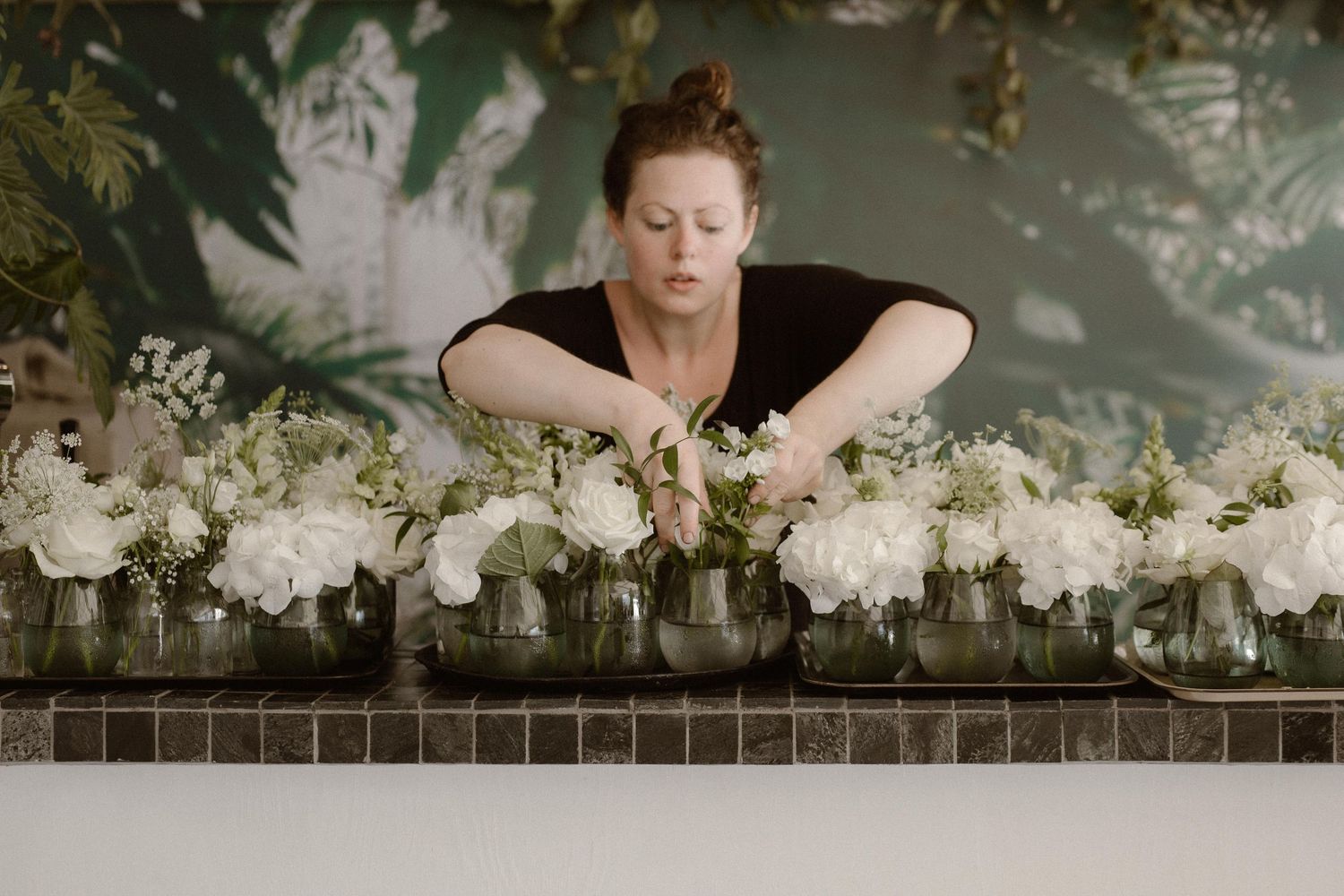 A florist arranging white floral decorations on a mantel or ledge.