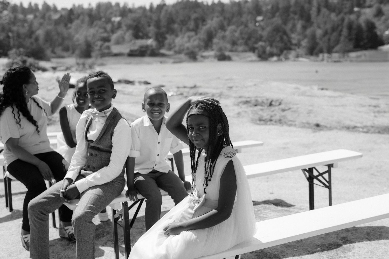 A black and white photo of wedding guests seated on benches at an outdoor event space.