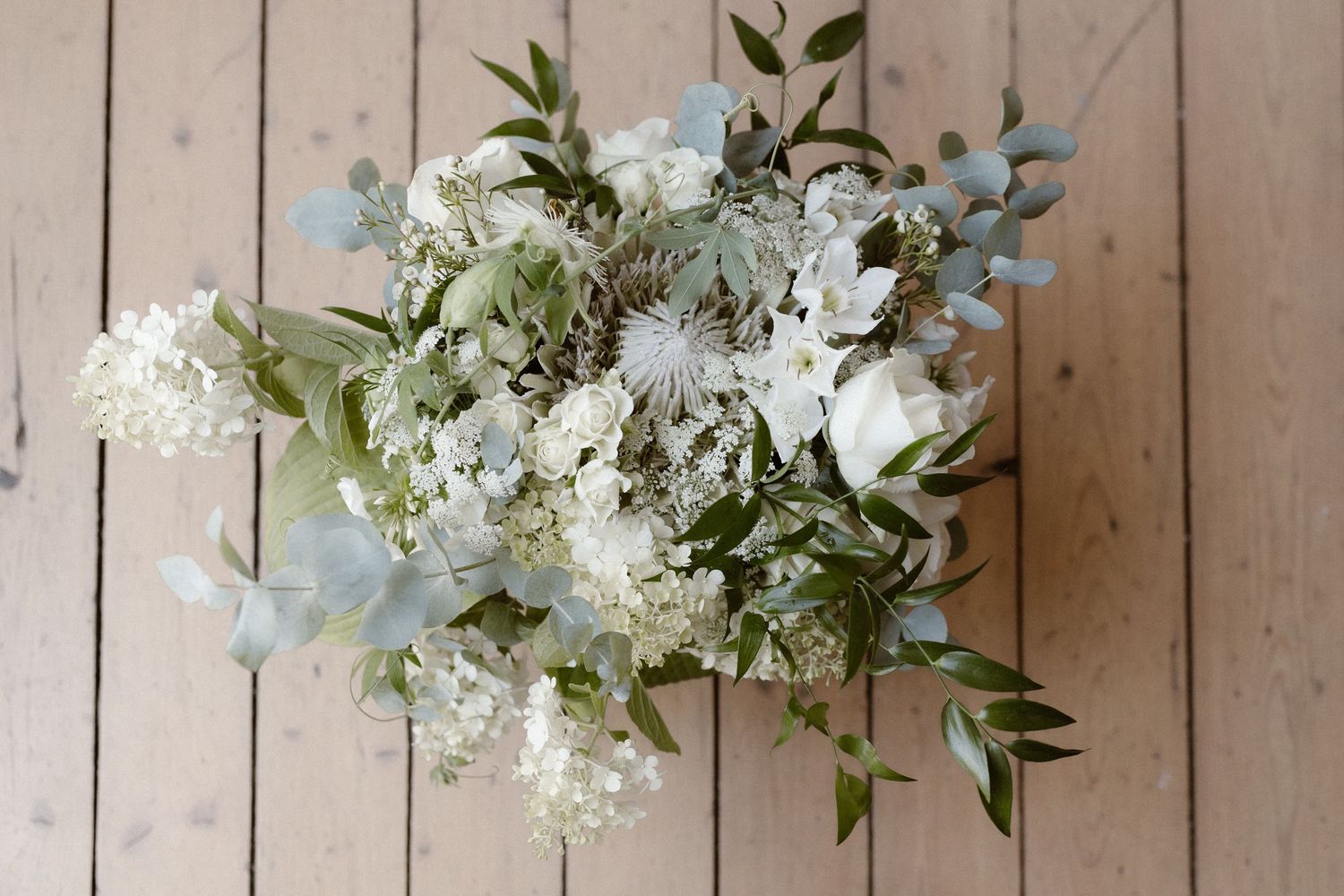 Elegant white and blue wedding bouquet with eucalyptus leaves on wooden floor.