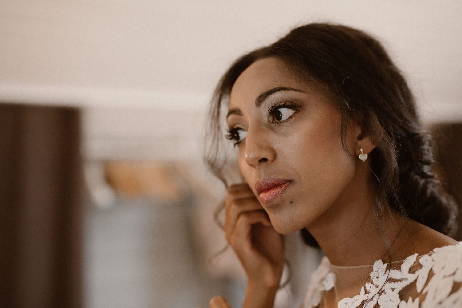 Woman in white lace wearing pearl earrings gazes thoughtfully to the side during preparation.