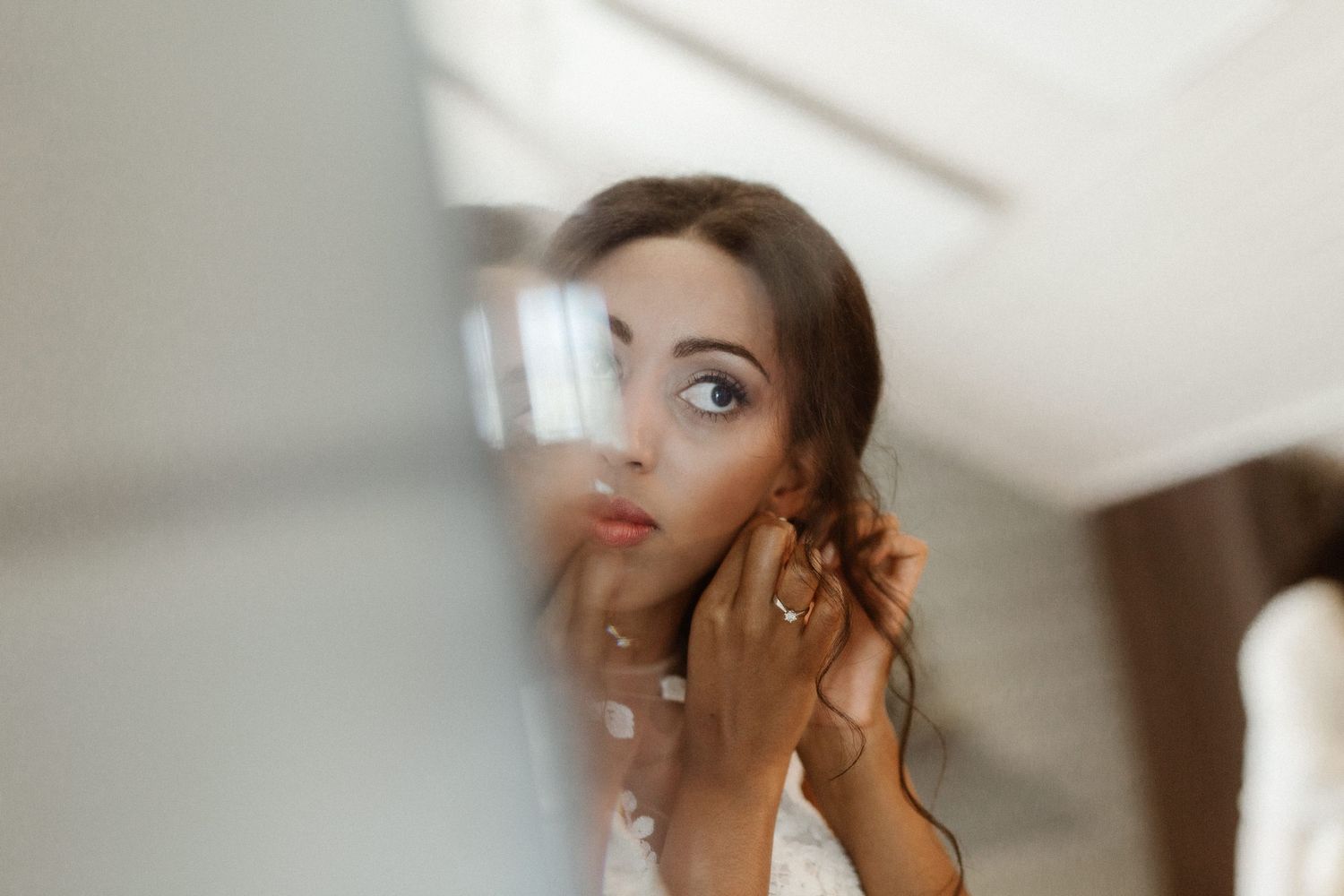 A soft-focused reflection in a mirror shows someone applying makeup with delicate hand movements.