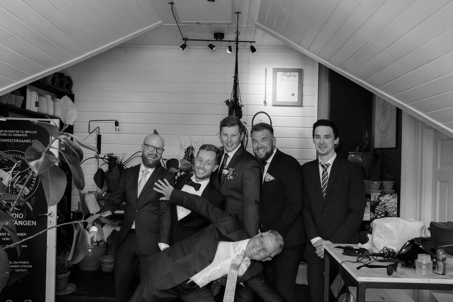 A black and white photograph of a group of people gathered in a small attic room with wood paneled walls.