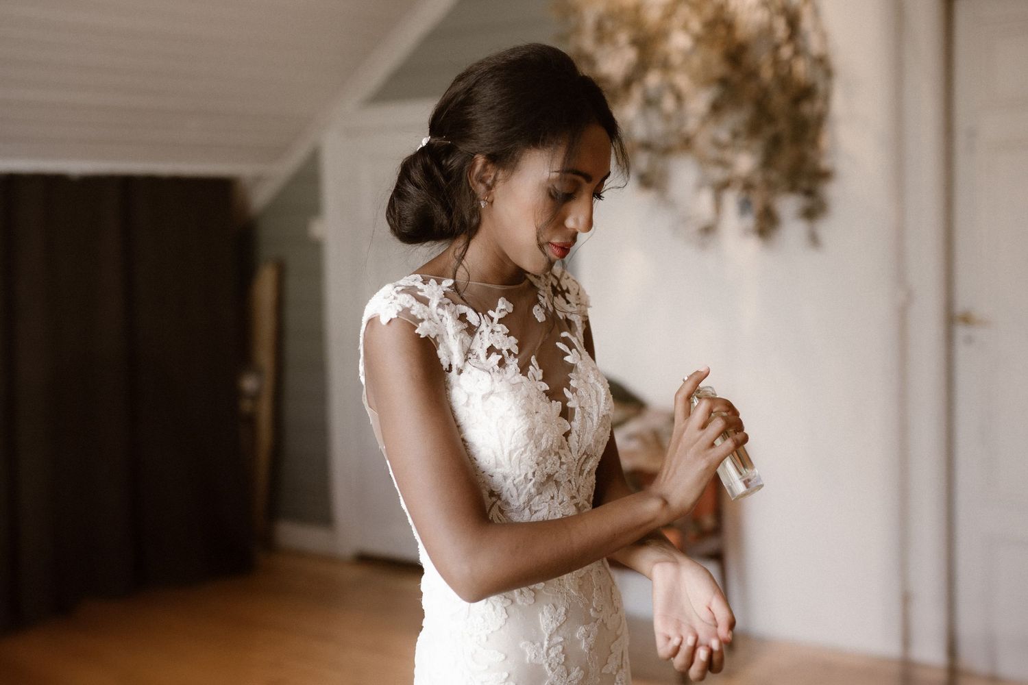 A delicate lace wedding dress being worn while adjusting a bracelet in a softly lit indoor setting.