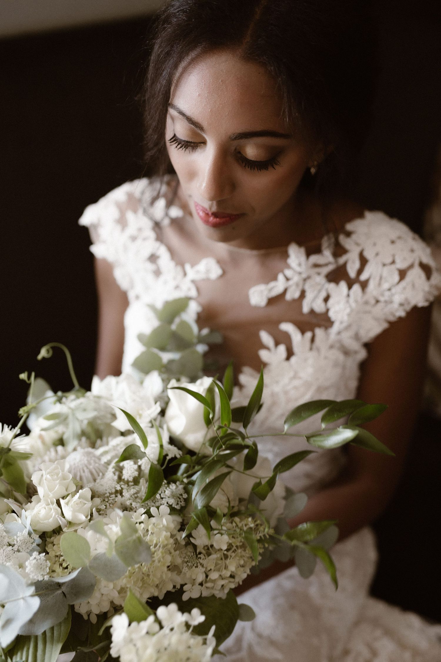 Bride in lace dress holding an elegant white and green floral bouquet.