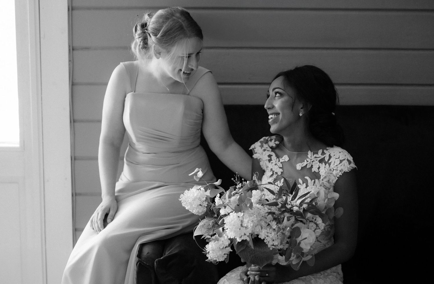 Two wedding party members sharing a joyful moment on a porch.