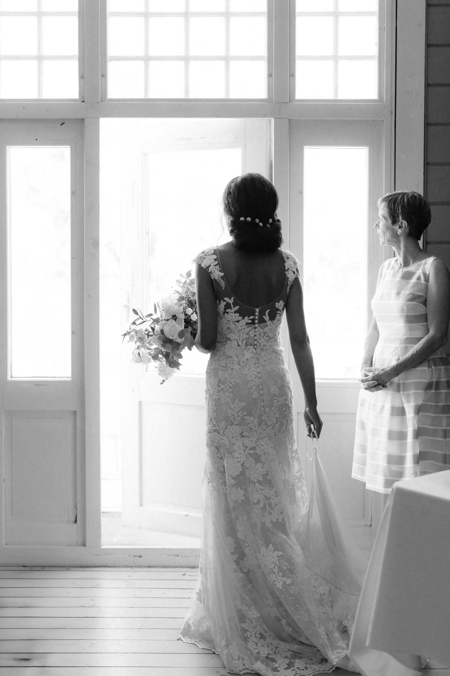 Silhouette of bride and companion standing by bright windows in an elegant room.