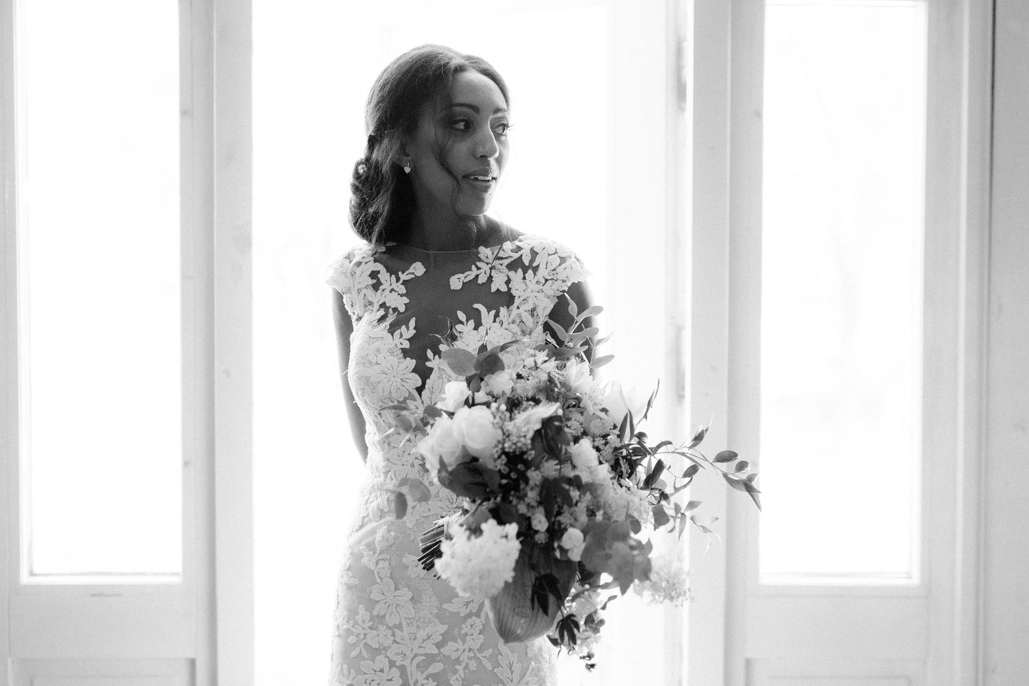 Black and white portrait of a bride with a luxurious bouquet by window light.