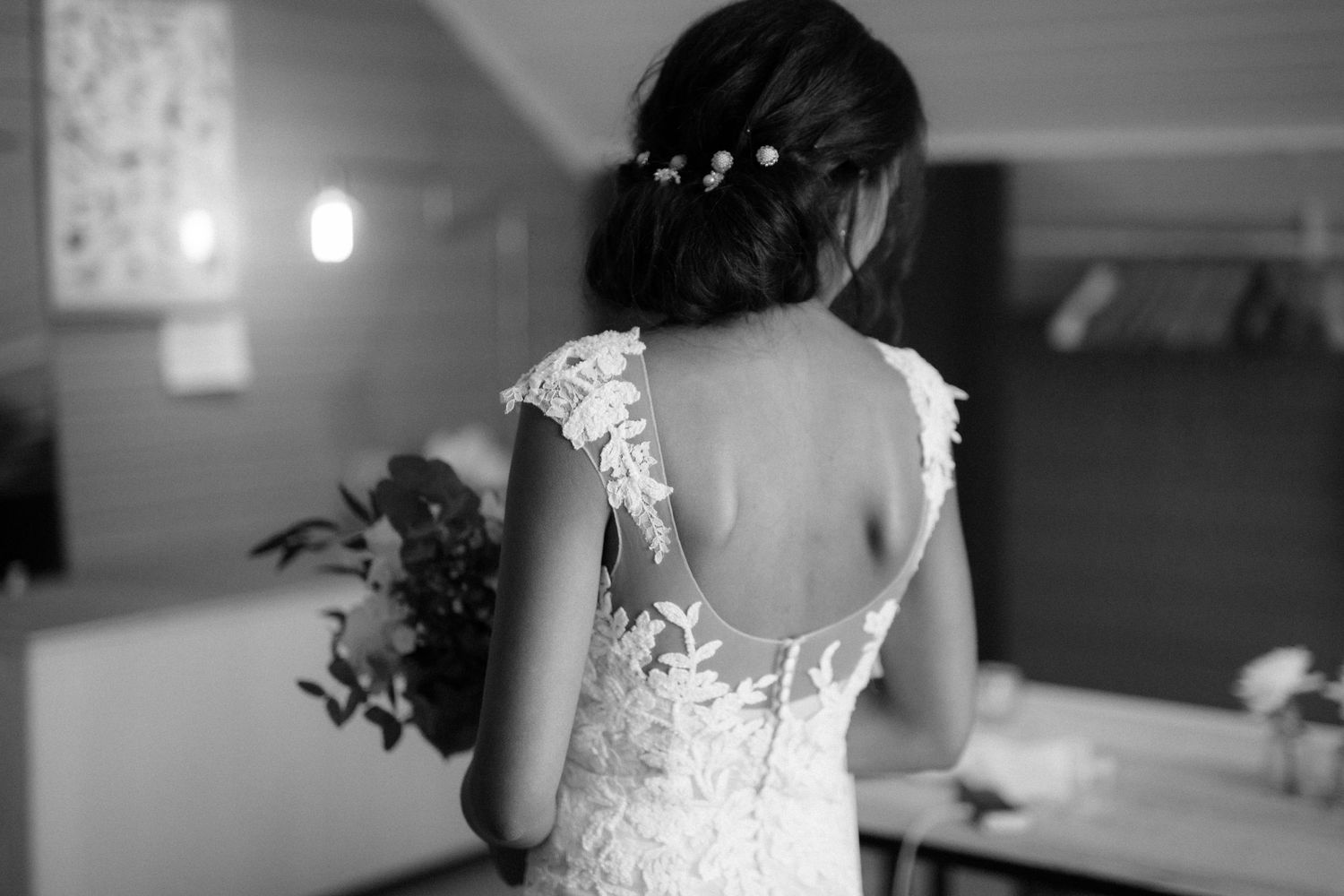 A black and white portrait showing the intricate lace back detail of a wedding dress.