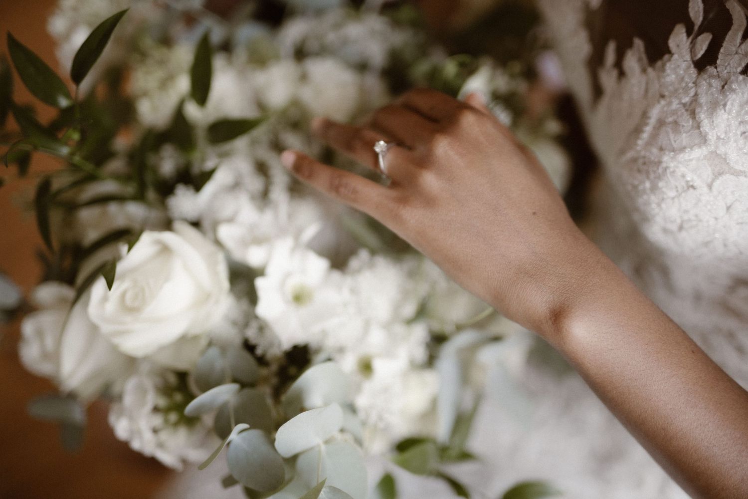 Someone's hand with an engagement ring reaches toward an elegant bouquet of white roses and flowers.