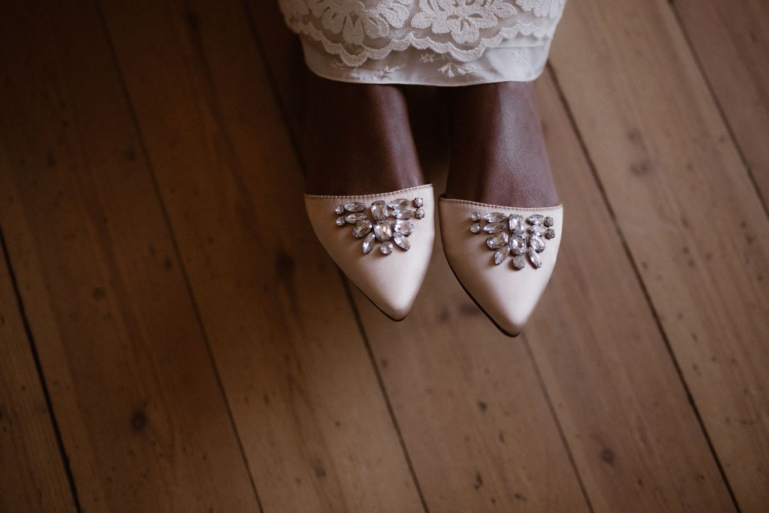 Close-up of embellished white bridal shoes on wooden floor.