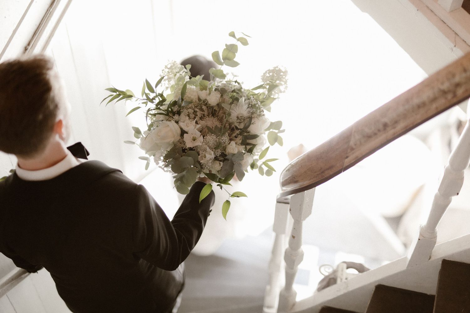 A sepia-toned photo shows someone holding a lush white and green wedding bouquet against a bright background.