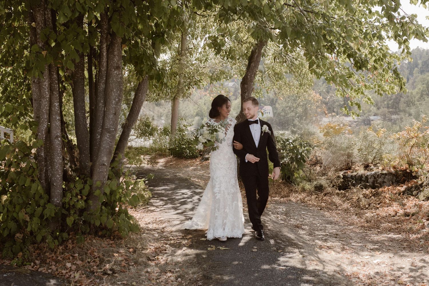 Romantic newlywed couple walking hand in hand on a tree-lined path during their outdoor wedding photoshoot.