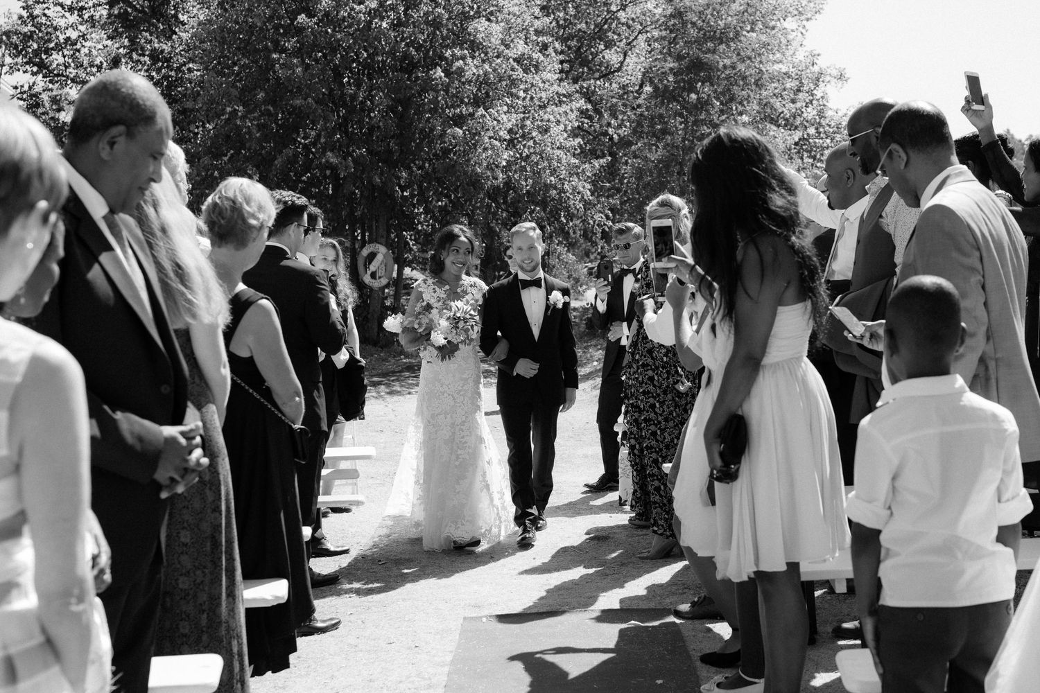 A black and white photograph of a wedding celebration with guests lining a path as rice is thrown at the happy couple.