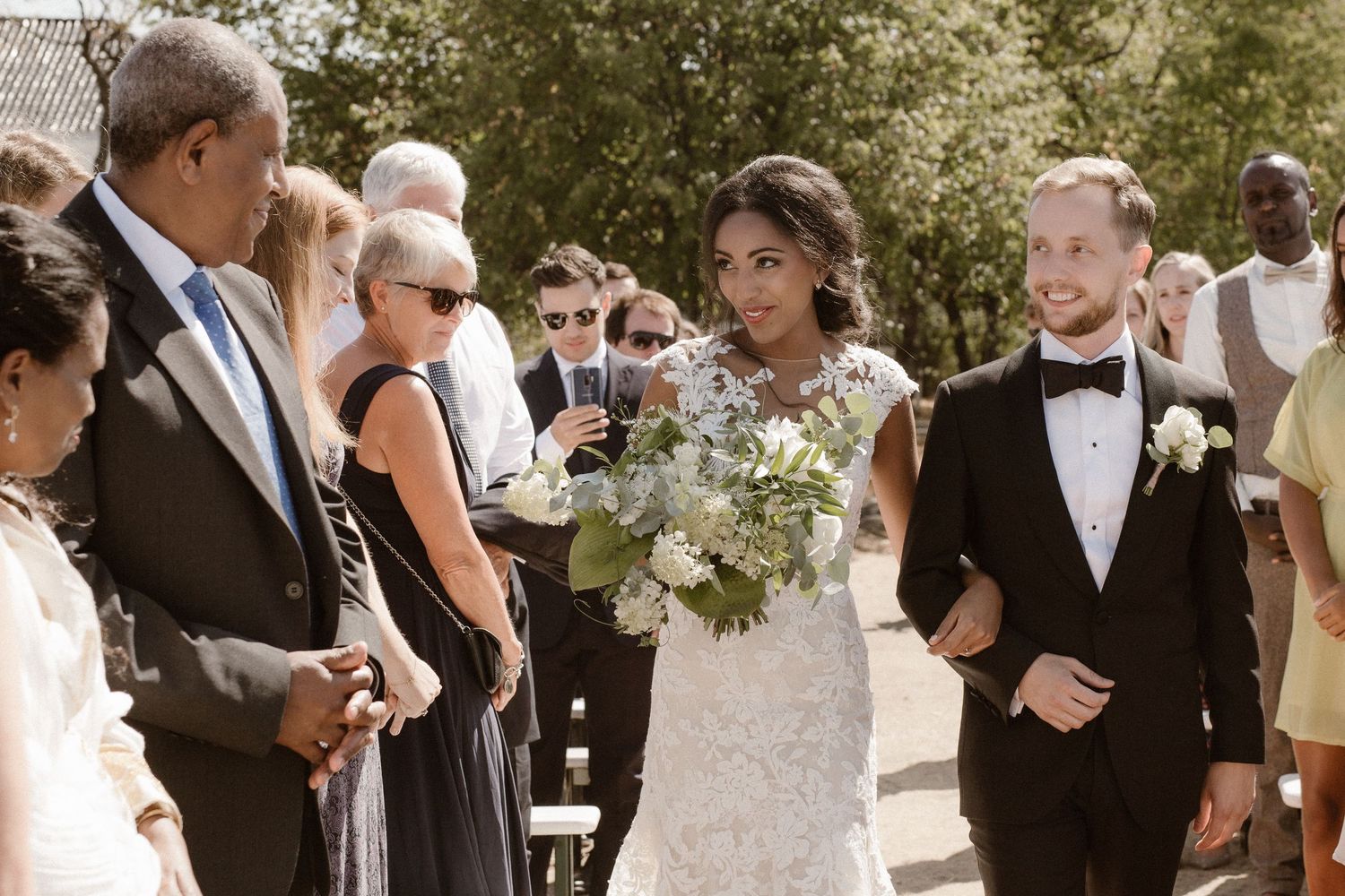 Wedding ceremony outdoors with couple and guests gathered in natural setting during sunny celebration.
