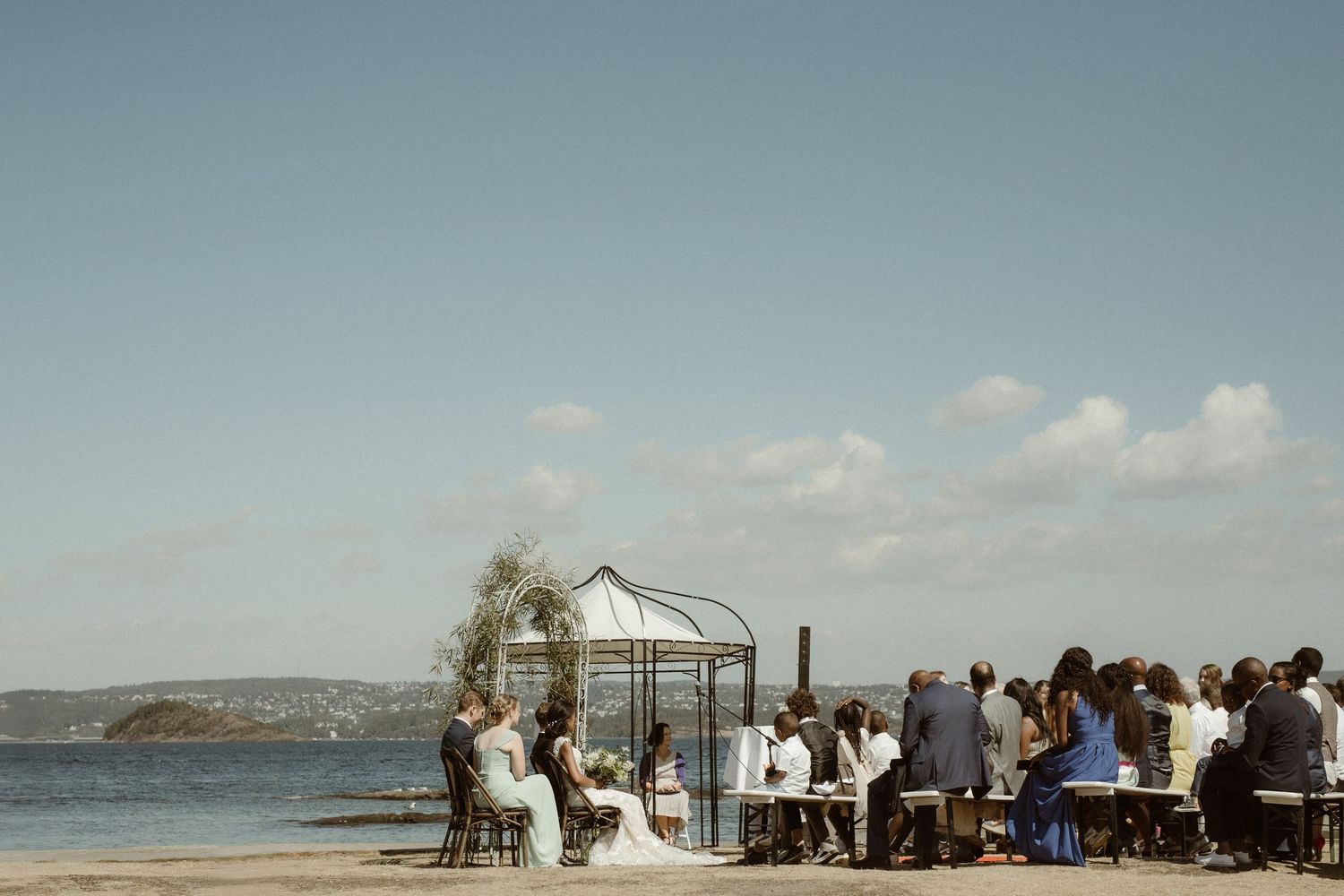A scenic beach wedding ceremony setup with chairs and a white arch overlooking the ocean on a sunny day.