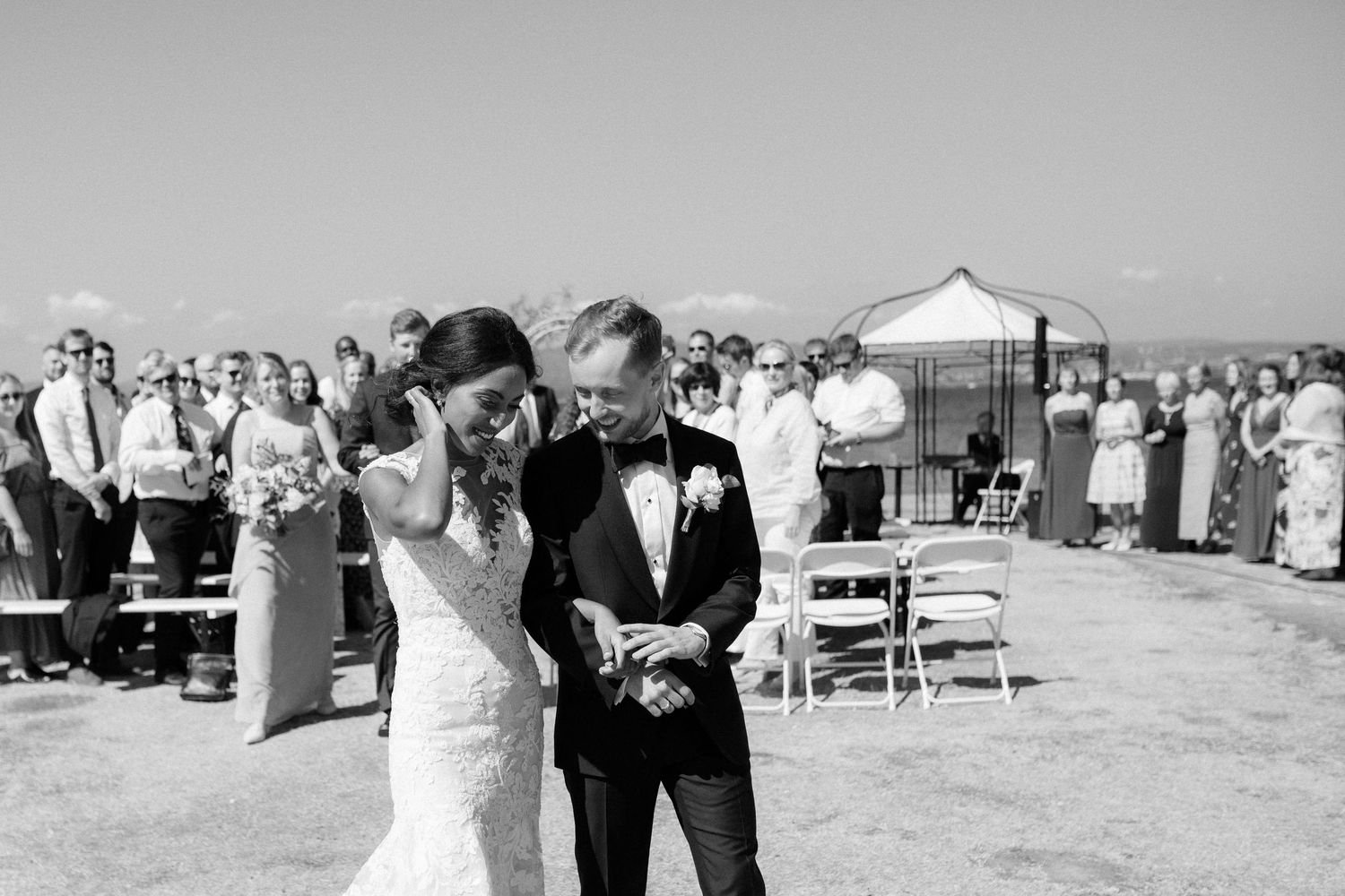 A couple shares a candid moment during their outdoor beach wedding ceremony surrounded by guests.