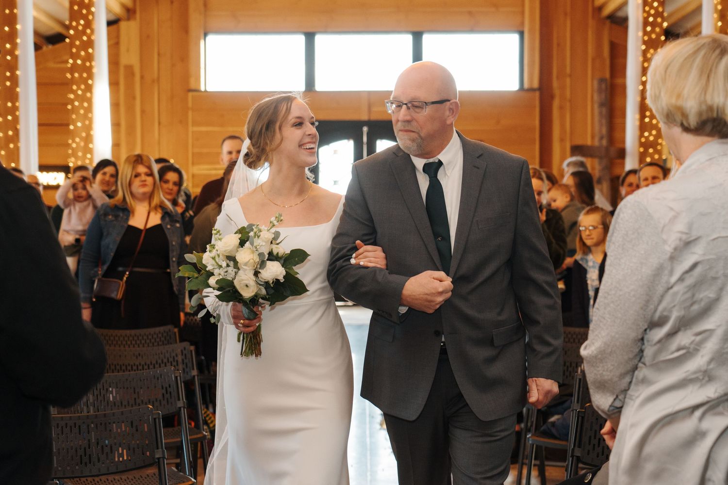 A traditional wedding ceremony takes place in a warm wooden church with sunlight streaming through windows.